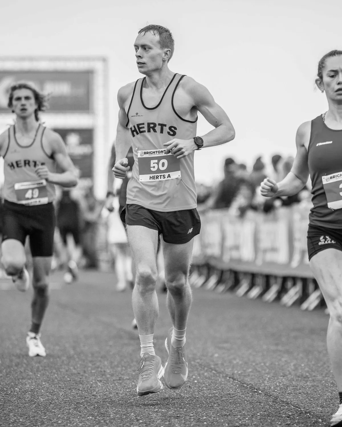 Black and white photograph of Matt racing the Brighton 10K in a Herts vest, bib number 50.